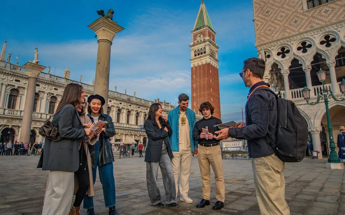 A guide explaining a building to two visitors in a small Venetian square